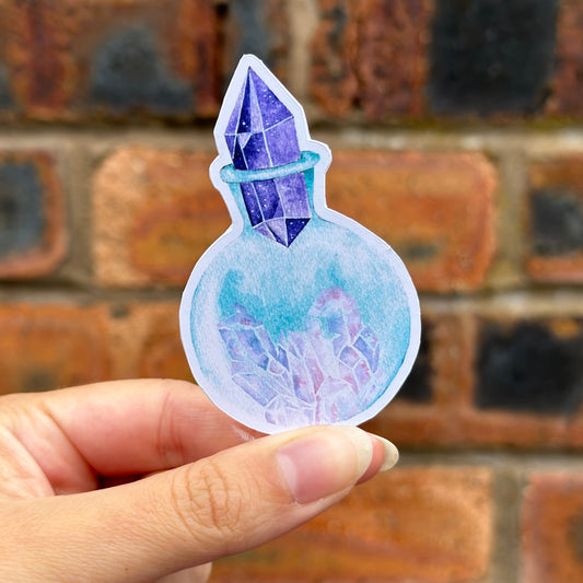 Hand holding a colorful crystal-like sticker against a textured wall background. Frontal