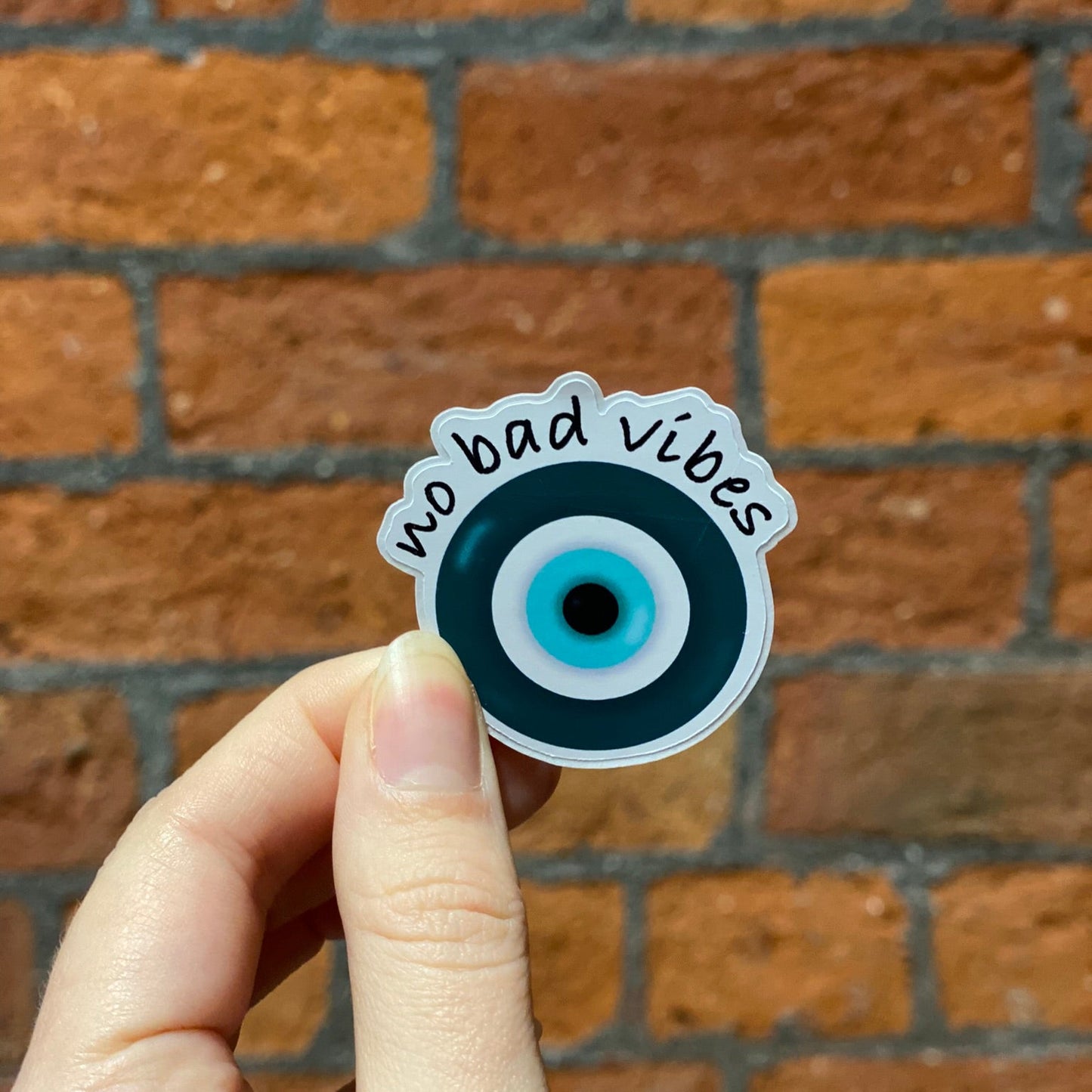 Aesthetic round matte sticker with a blue and black evil eye design and the text 'no bad vibes' . Frontal