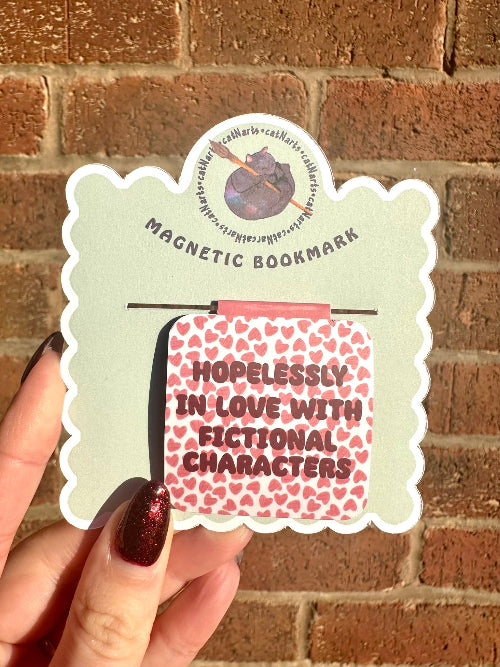 Magnetic bookmark with 'Hopelessly in Love with Fictional Characters' text held against a brick wall.