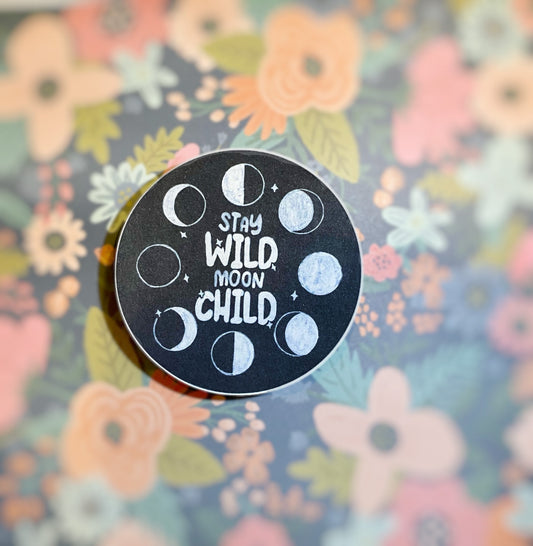 Black round celestial sticker with matte finish, moon phaes and text 'stay wild moon child'. Frontal