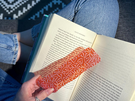 A handmade transparent bookmark with a red background, white heart patterns and wavy edge on open book