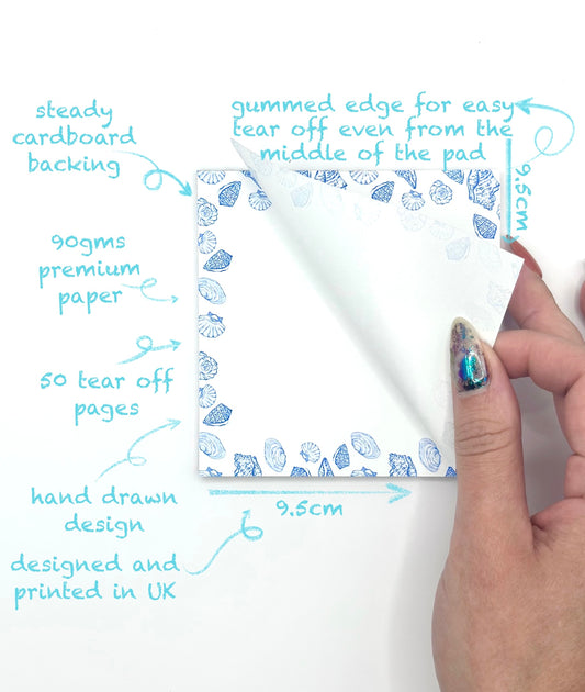 Square memo pad with tear-off pages and a hand-drawn blue coastal design, held by a hand.