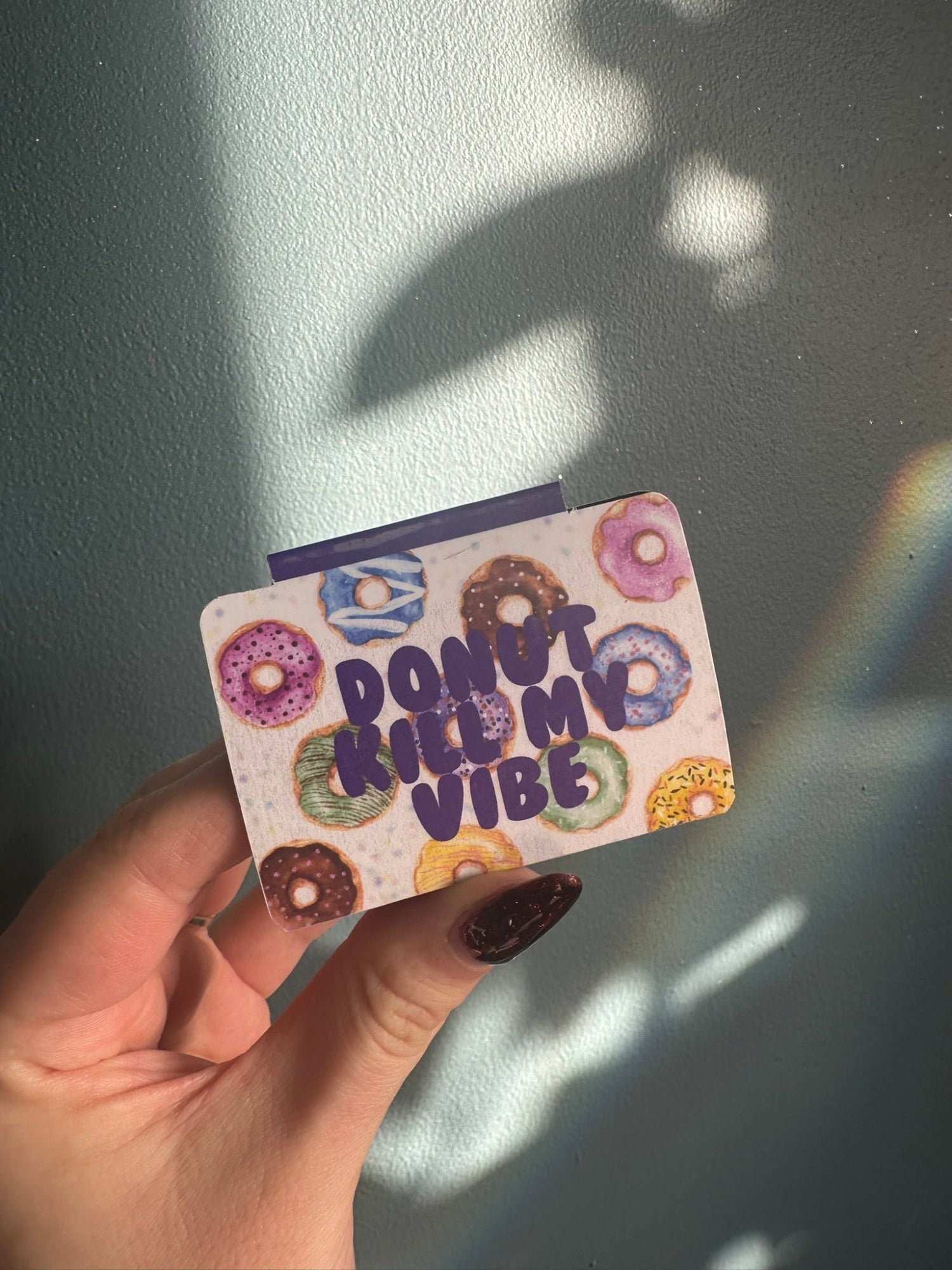 Hand holding a magnetic bookmark with colorful donut designs and 'Don't Kill My Vibe' text against a light background.