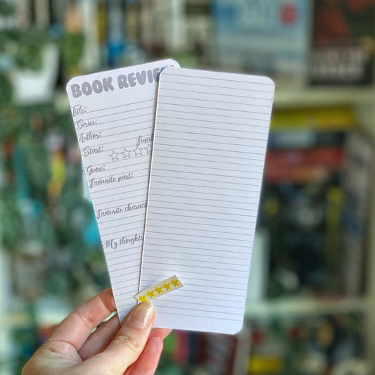 A hand holding a double-sided bookmark with lined areas for notes and a set of yellow star stickers for rating, with a blurred background of books.