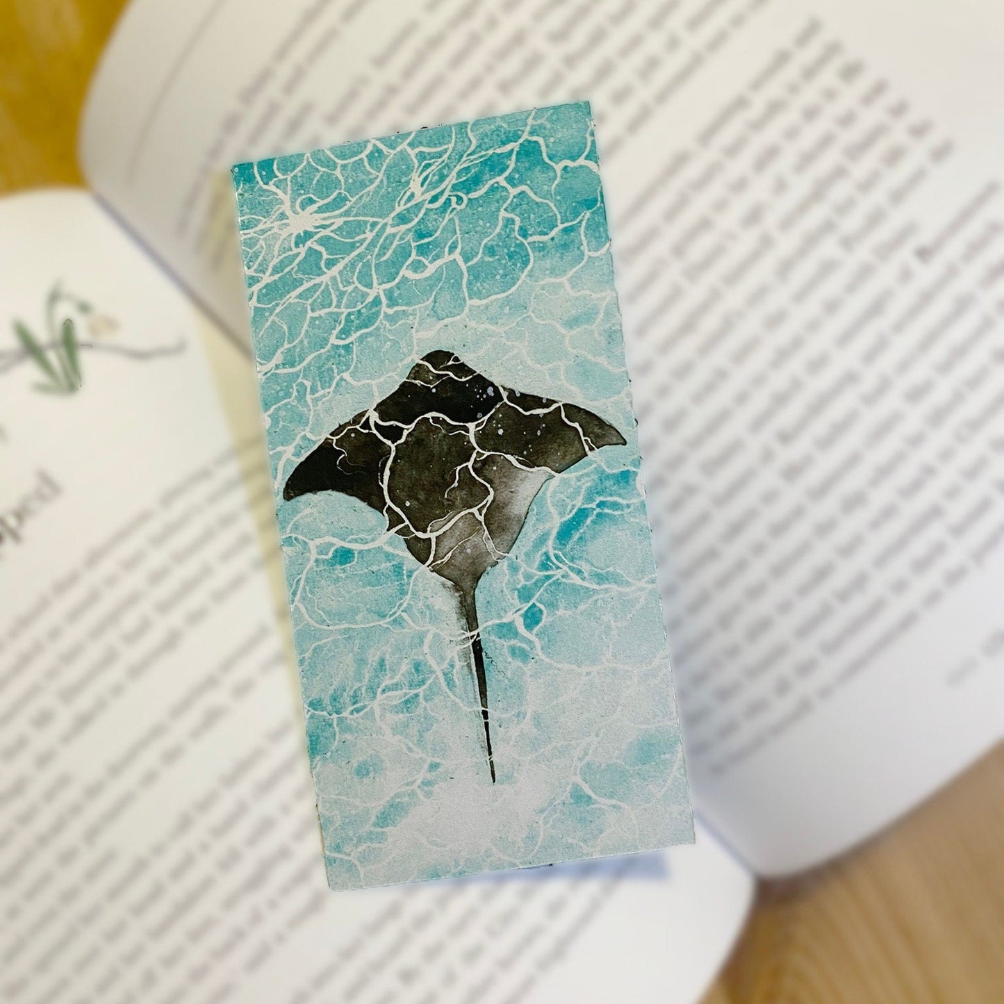 A glossy bookmark with a marine ray fish design, on top of a book. Top view