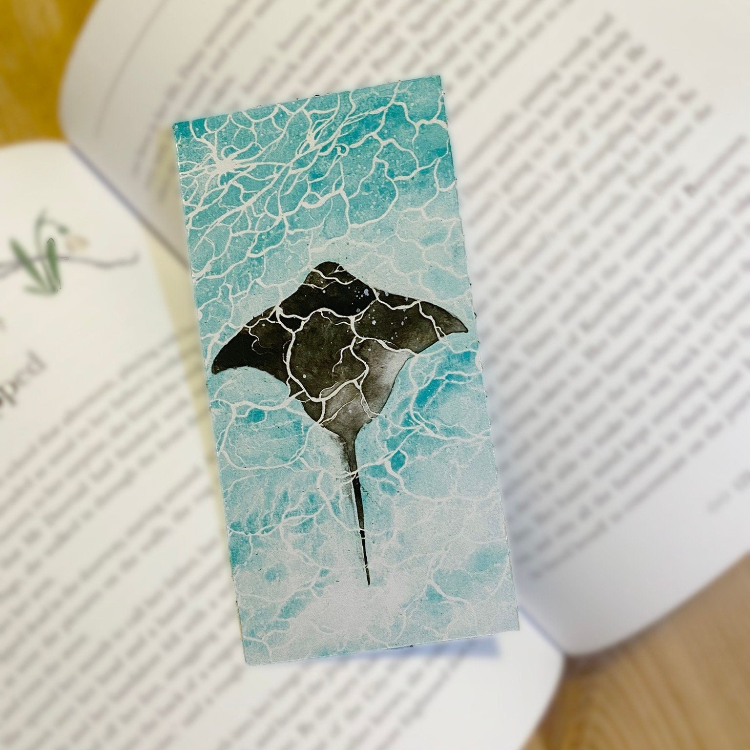 A glossy bookmark with a marine ray fish design, on top of a book. Top view