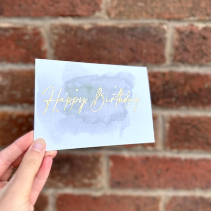 Aesthetic birthday card on watercolour background and gold detail text 'happy birthday'. Frontal 