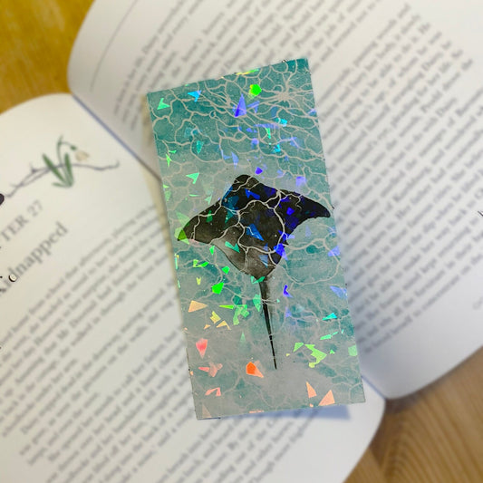 Holographic finish bookmark with a marine ray fish design, on top of a book. Top view