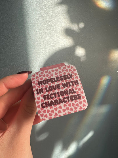 Magnetic bookmark with text 'Hopelessly in love with fictional characters' hold agains a light background