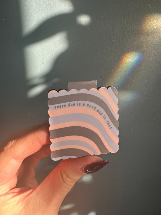 Colorful magnetic bookmark with text 'every day is a good day to read' held by a hand against a dark backgroun