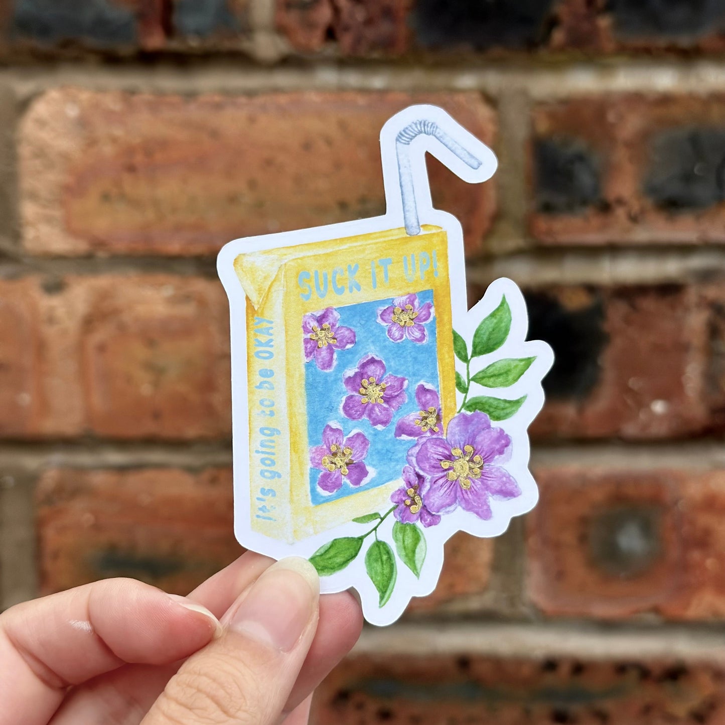 Aesthetic motivation sticker resempling juice cartoon with text 'suck it up! it's going tobe okay' and floral motives. Frontal