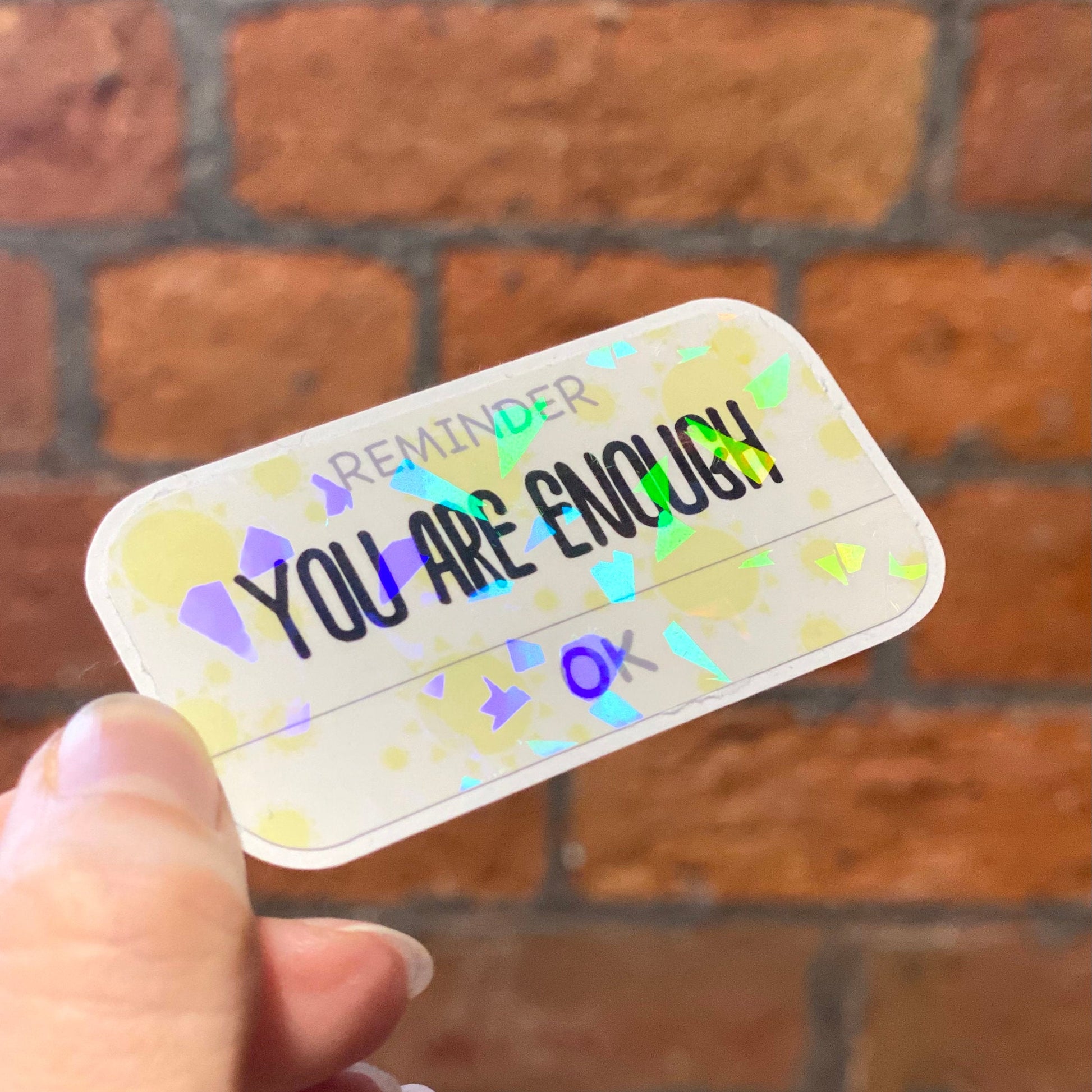 Holographic aesthetic motivation sticker with text 'reminder you are enough'. Angle view