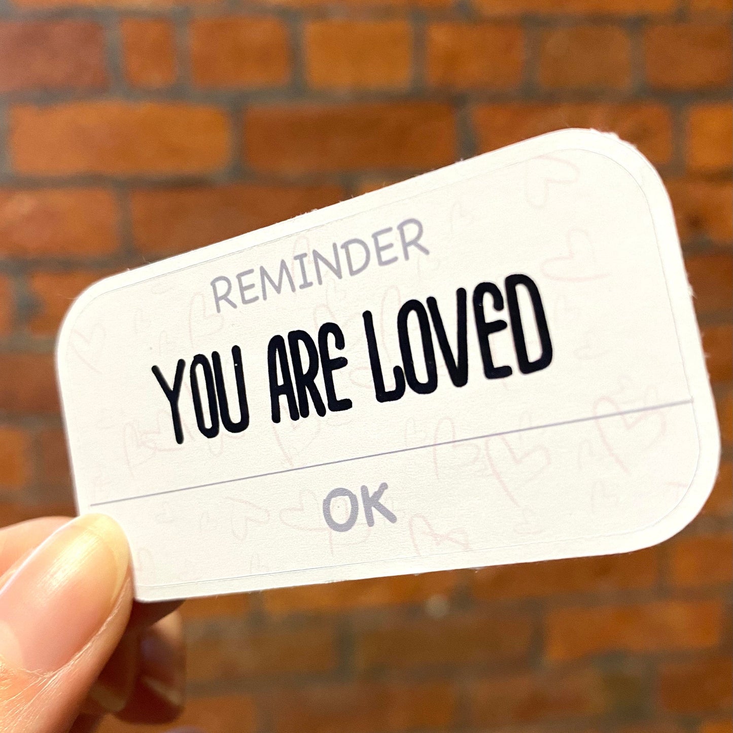 Pink motivation sticker with the text 'YOU ARE LOVED' . Angle view