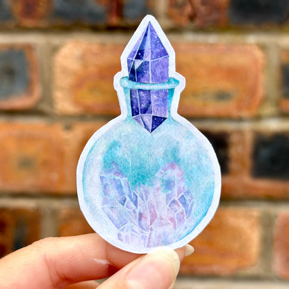 Sticker of a crystal in a potion bottle held against a brick wall. Frontal