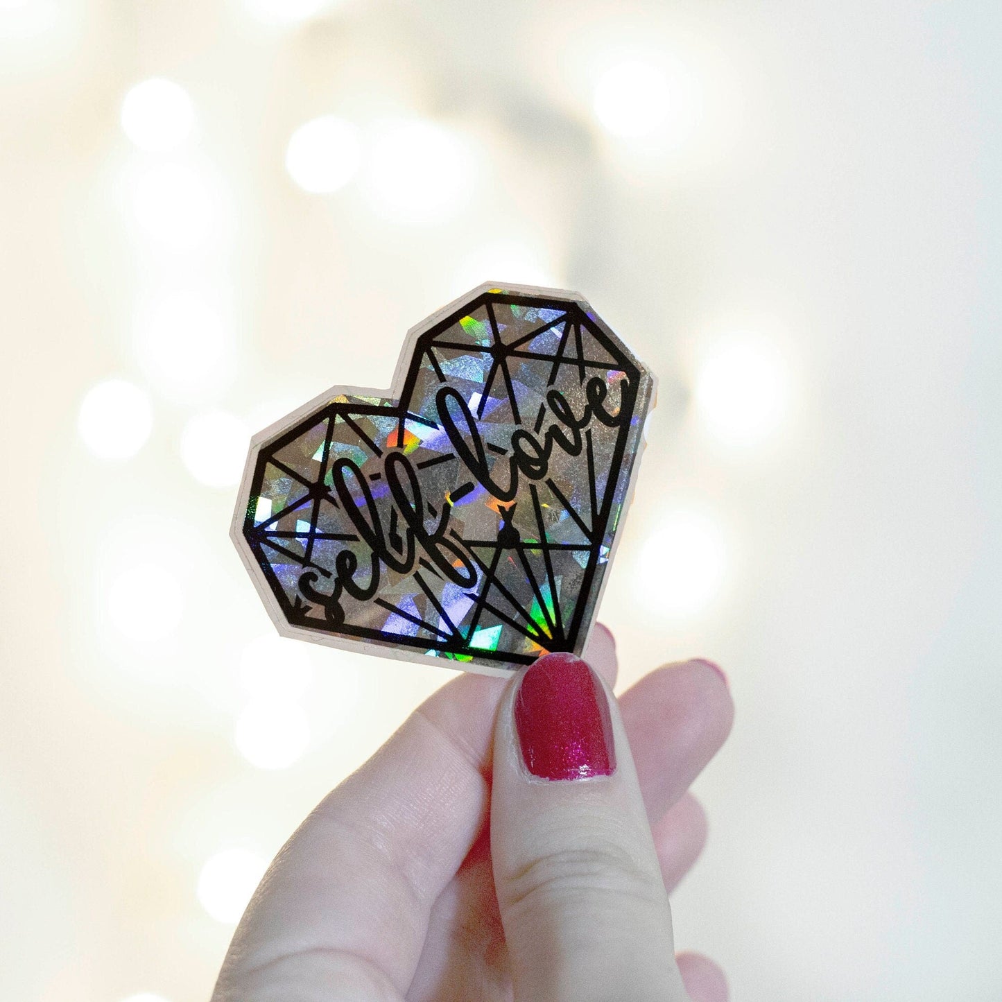 A holographic sticker with a geometric heart pattern with 'self love' text
