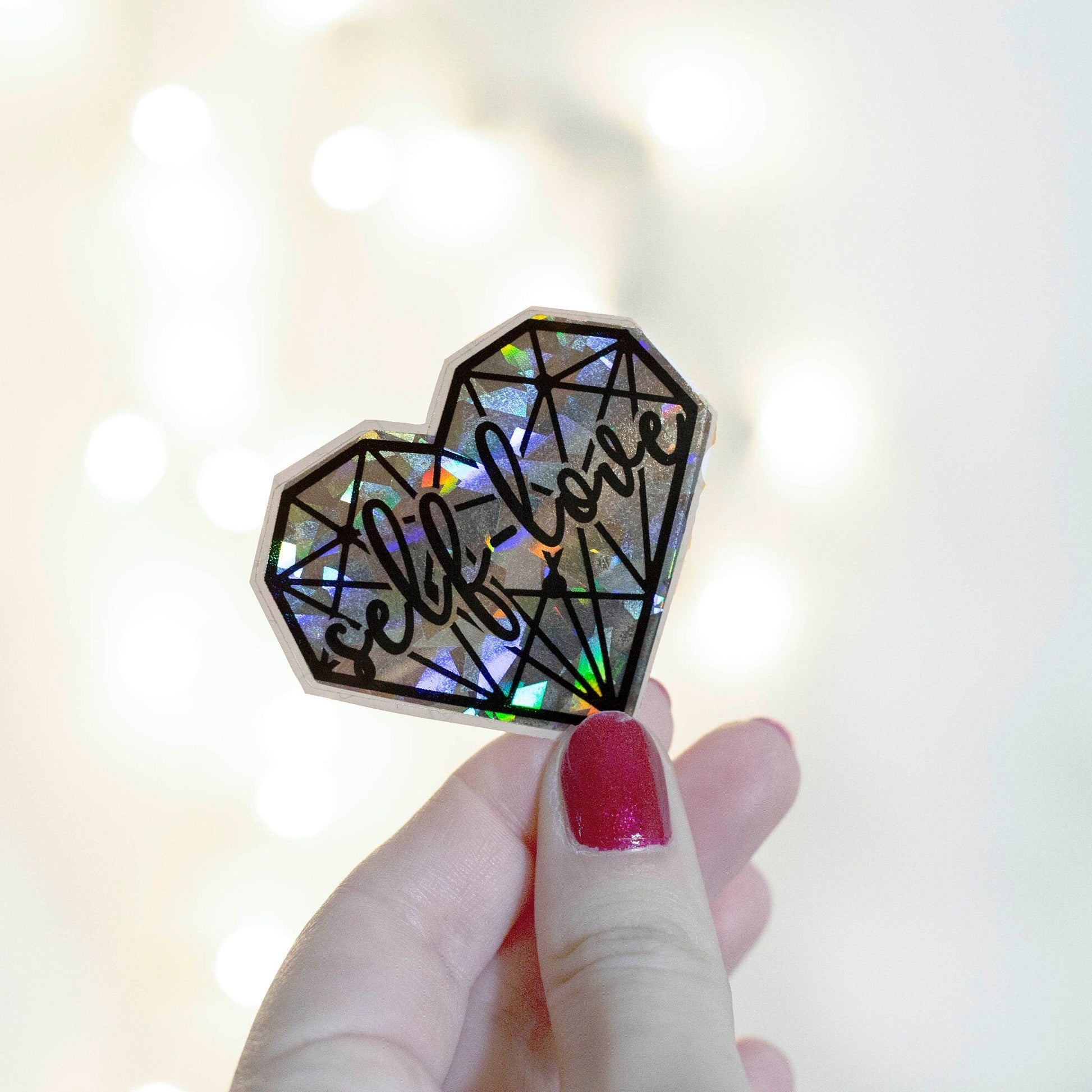 A holographic sticker with a geometric heart pattern with 'self love' text