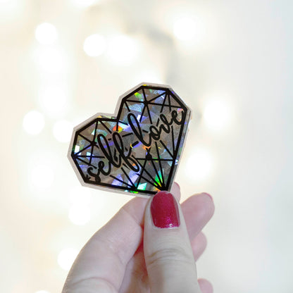 A holographic sticker with a geometric heart pattern with 'self love' text