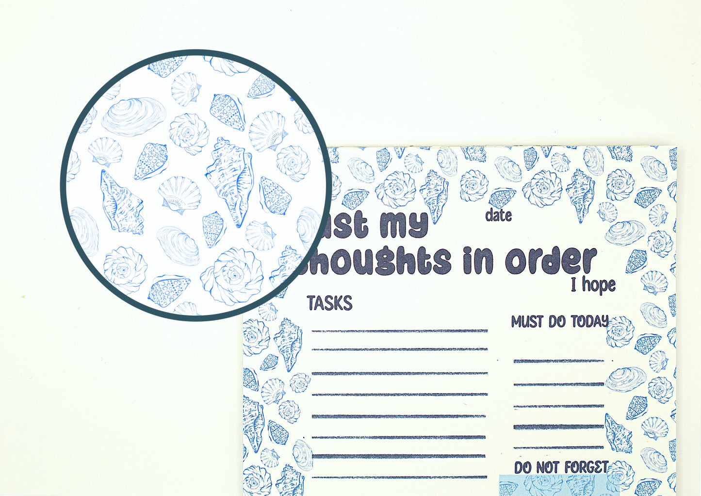 A notepad with a blue seashell pattern on a white background, featuring a circular magnified inset showing the detailed shell print.