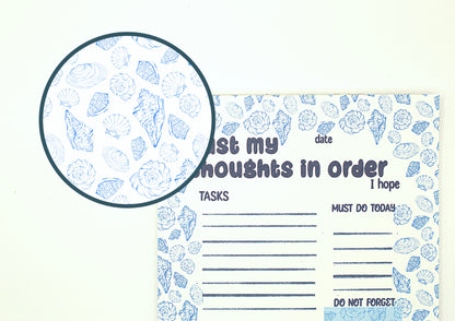 A notepad with a blue seashell pattern on a white background, featuring a circular magnified inset showing the detailed shell print.