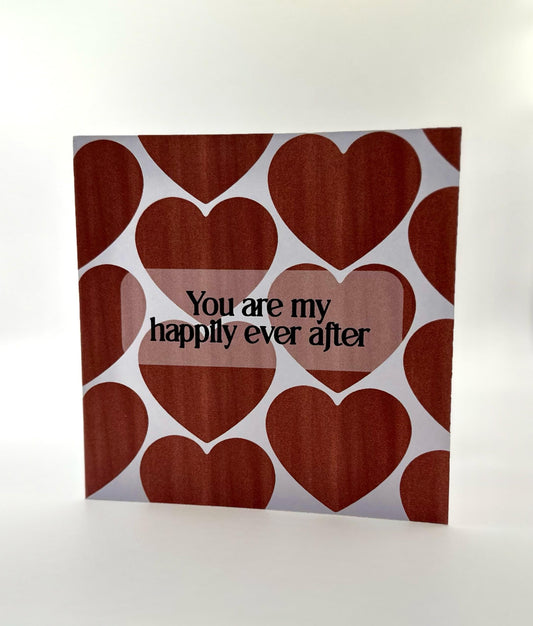 A Valentine's Day card with a heart pattern and the text 'You are my happily ever after' printed on the front. The card is white with red hearts and a visible envelope slot.