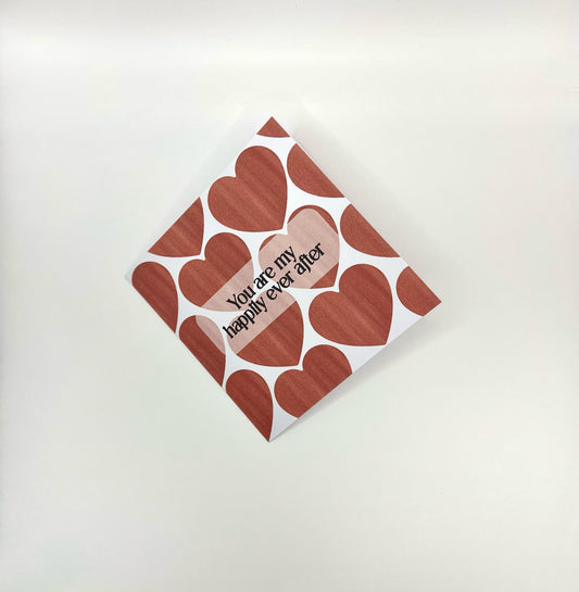A Valentine's Day card with a heart pattern and the text 'You are my happily ever after' printed on the front. The card is white with red hearts and a visible envelope slot.