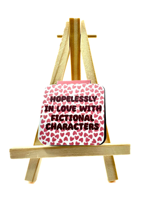 Square magnetic bookmark with heart patterns and text 'Hopelessly in love with fictional characters' on a wooden easel against a white background