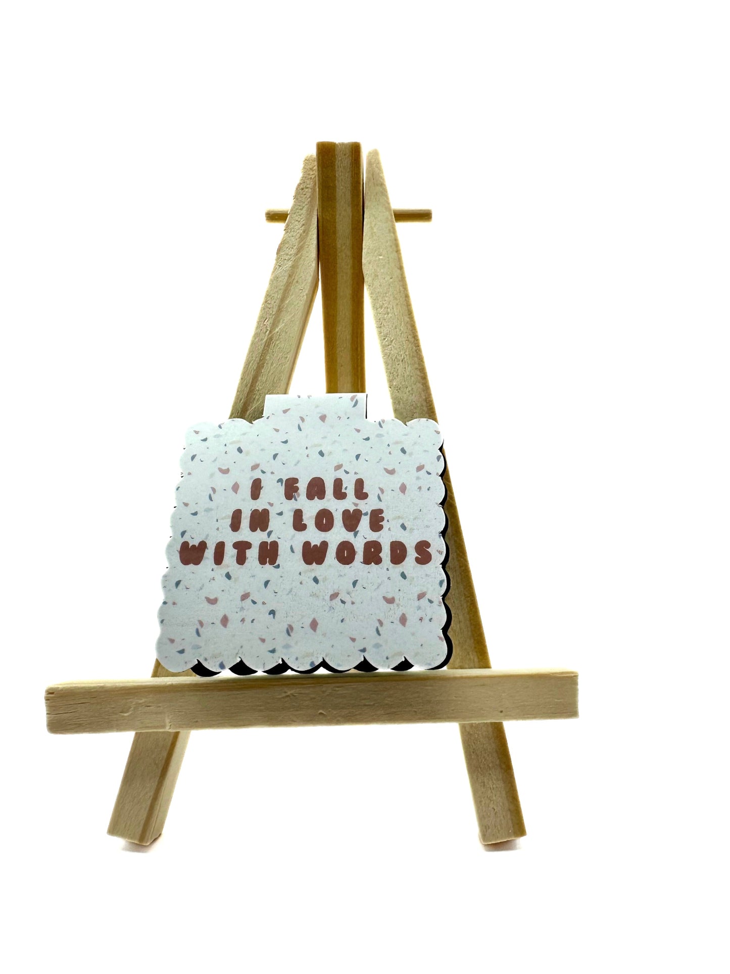 Small terrazzo style magnetic bookmark with 'I fall in love with words' text on a wooden easel against a white background