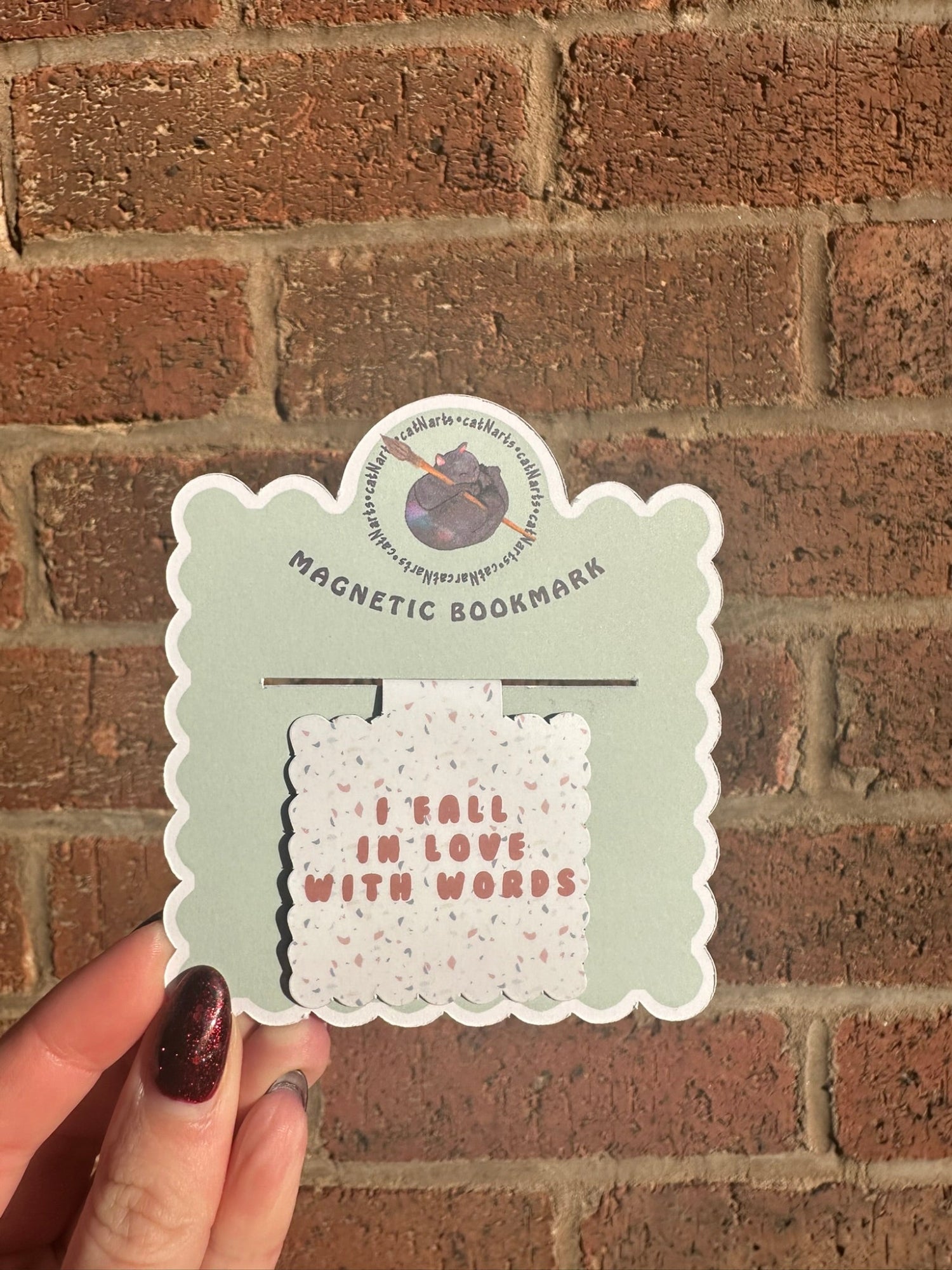 Magnetic bookmark with 'I fall in love with words' text held against a brick wall.