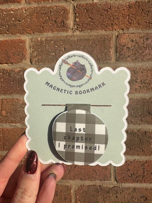 Magnetic bookmark with checkered design and text held against a brick wall