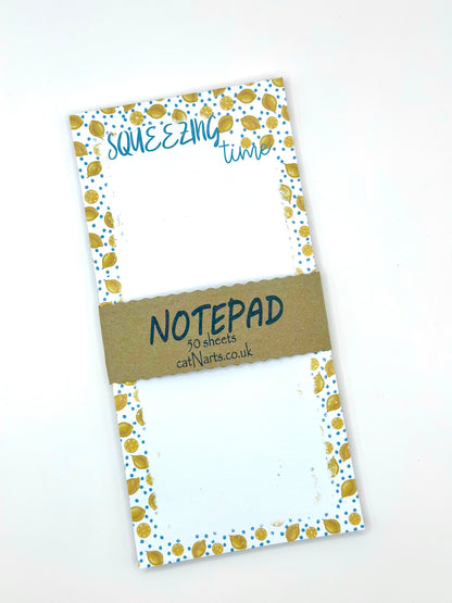 Notepad with a white background, blue flowers and lemons patterned edges. The top reads 'SQUEEZING time' in blue script, and a brown paper band across the center reads 'NOTEPAD 50 sheets callNarts.