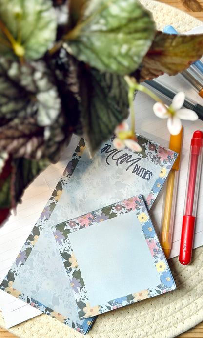 Floral notepad on a desk with stationery items and a plant.