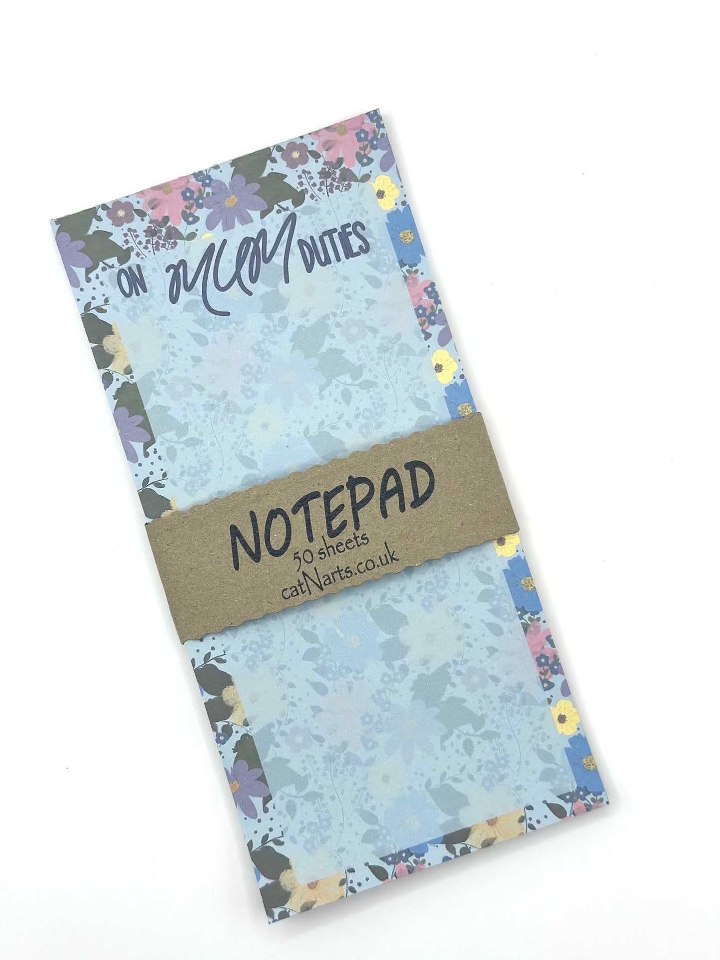 A floral-patterned notepad with a text 'on mum duties' with a brown paper band reading 'NOTEPAD' and '50 sheets 