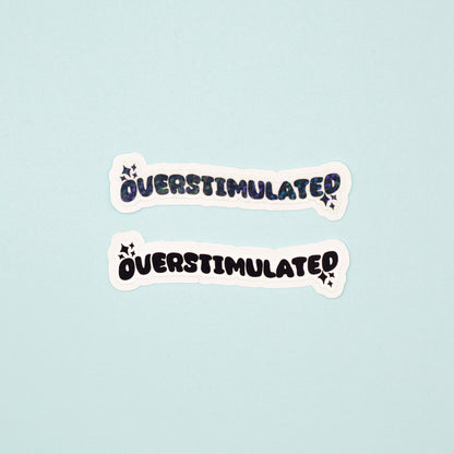 Two die-cut stickers with the word 'OVERSTIMULATED' in a black bubbly font pne matte, one with a holographic dot overlay, displayed on a light blue background.