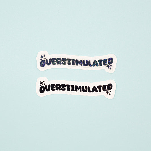 Two die-cut stickers with the word 'OVERSTIMULATED' in a black bubbly font pne matte, one with a holographic dot overlay, displayed on a light blue background.