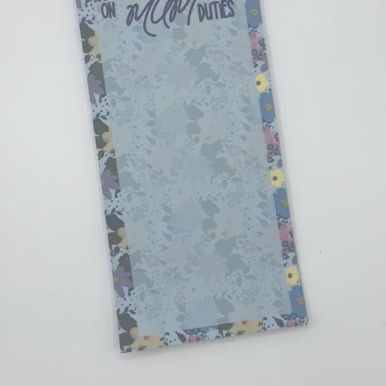 A vertical memo pad with a floral-patterned border and a light blue floral center. The top reads 'ON MUM DUTIES' in stylised lettering.