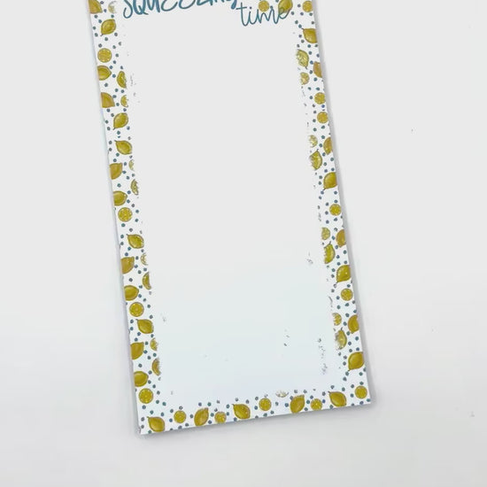 Notepad with a white background, blue flowers and lemons patterned edges. The top reads 'SQUEEZING time' in blue script, and a brown paper band across the center reads 'NOTEPAD 50 sheets callNarts.