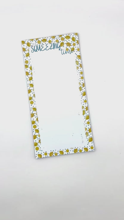 Notepad with a white background, blue flowers and lemons patterned edges. The top reads 'SQUEEZING time' in blue script, and a brown paper band across the center reads 'NOTEPAD 50 sheets callNarts.