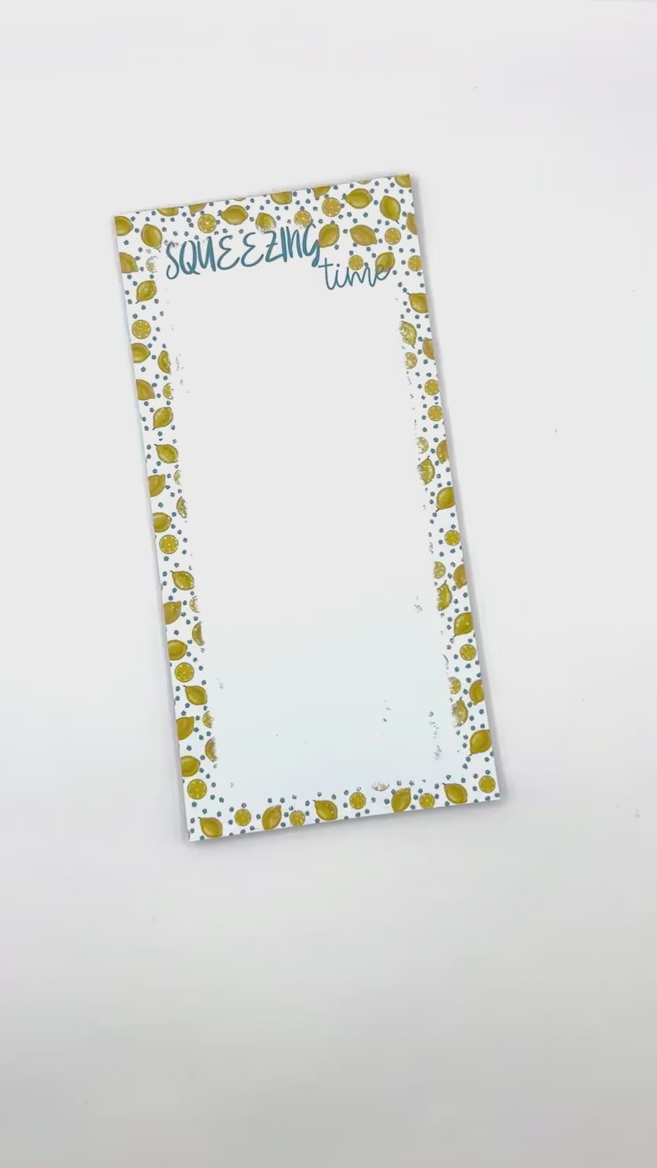Notepad with a white background, blue flowers and lemons patterned edges. The top reads 'SQUEEZING time' in blue script, and a brown paper band across the center reads 'NOTEPAD 50 sheets callNarts.