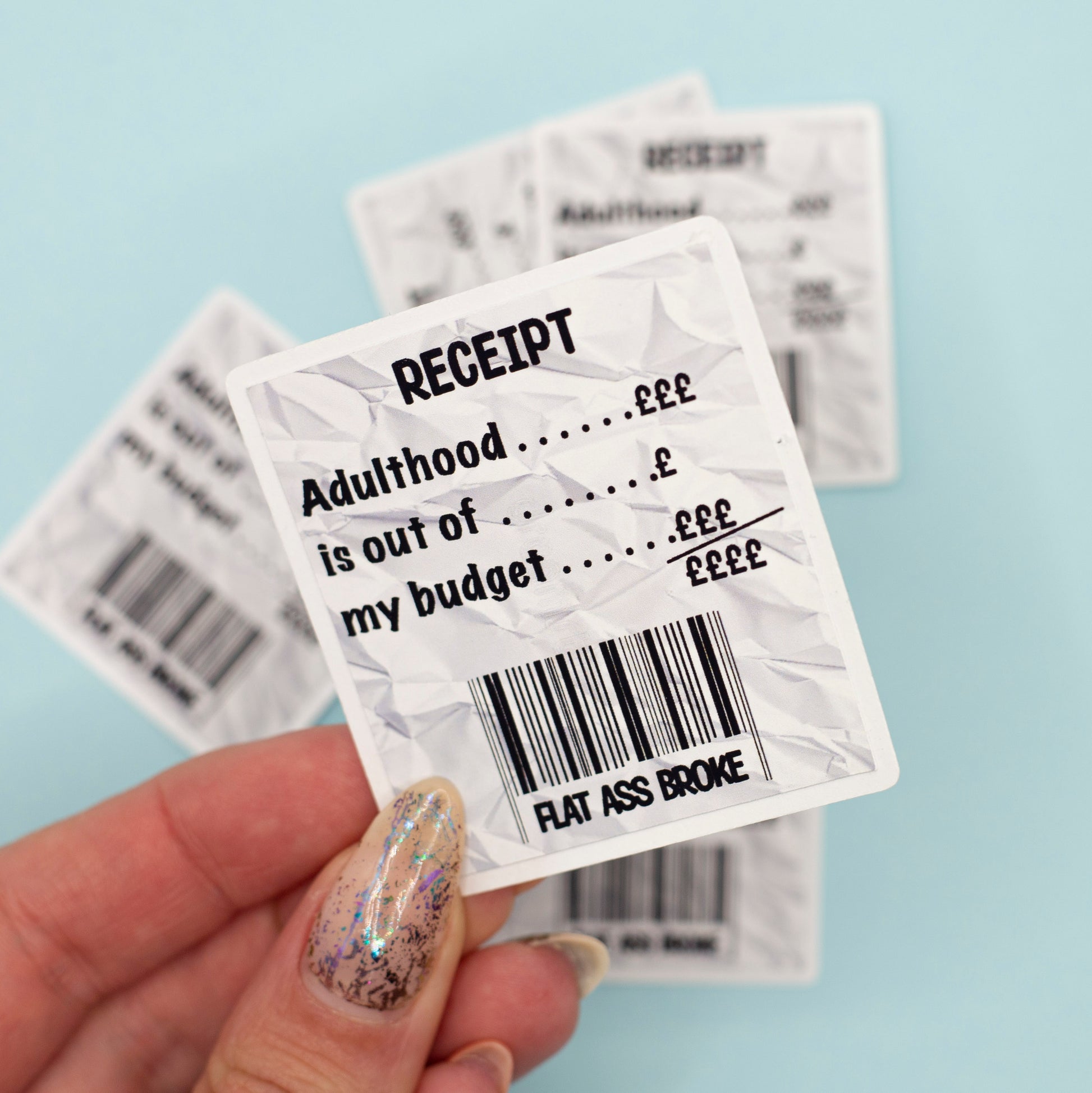A crumpled white receipt-style sticker with black text reading 'RECEIPT Adulthood is out of my budget flat ass broke'.