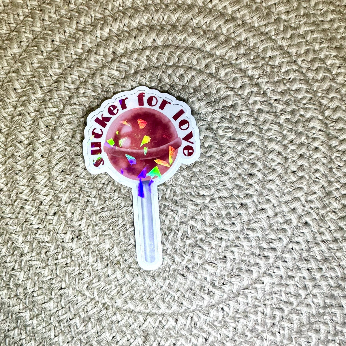 Sticker of a lollipop with 'sucker for love' text on a textured beige background