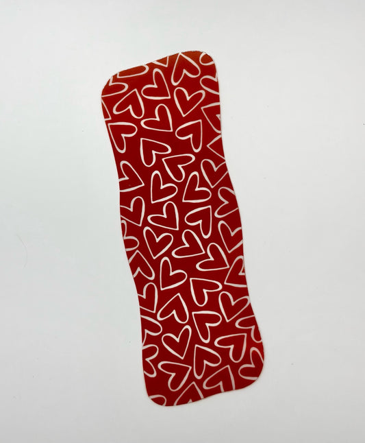 A handmade transparent bookmark with a red background, white heart patterns and wavy edge.